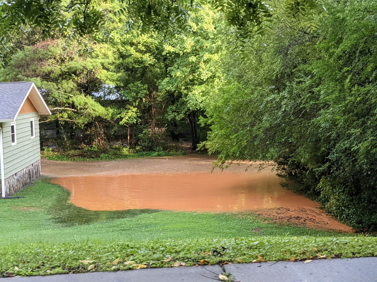 Pale green house on left side of frame, backyard full of brown flood waters